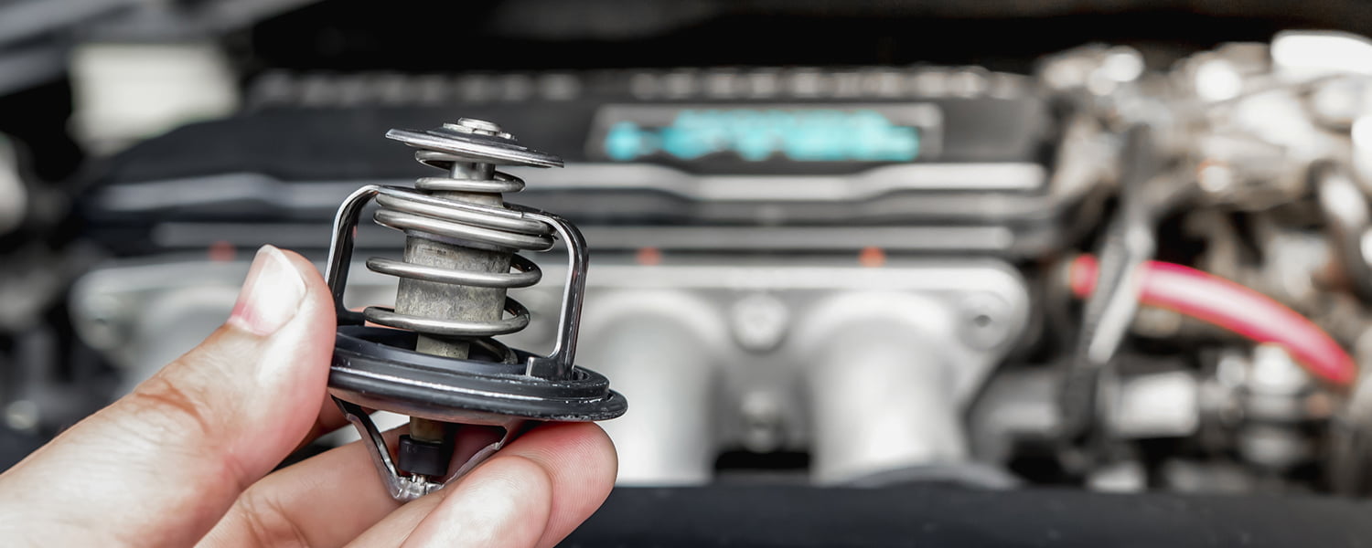 Coolant thermostat held beside an engine