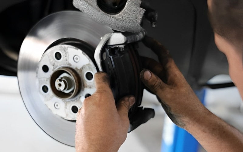 Technician working on a brake caliper beside the exposed disc