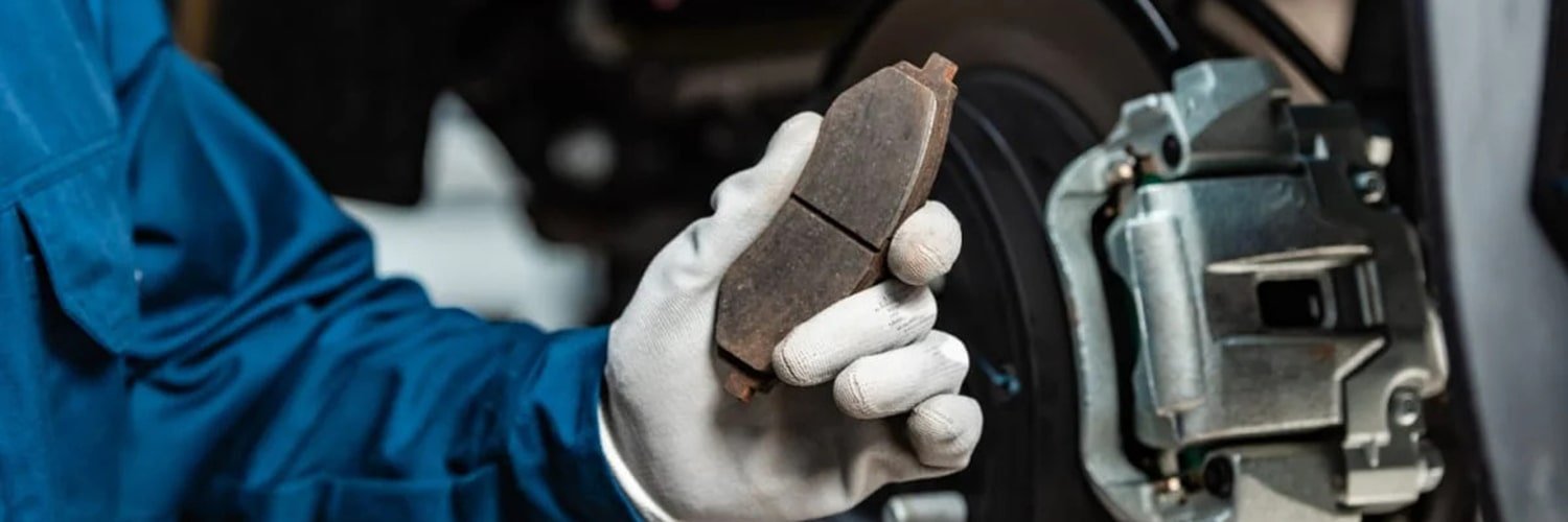 Gloved technician holding a brake pad beside the caliper