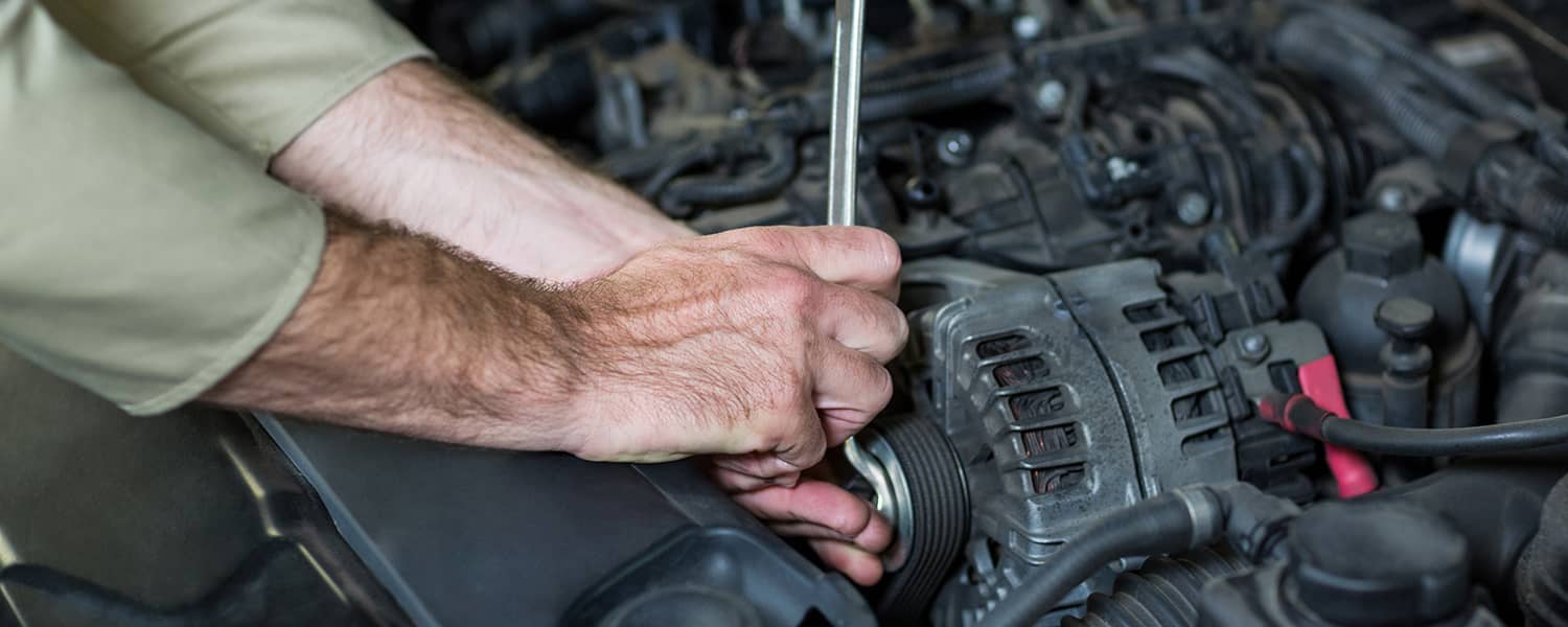 Technician working at the alternator and drive pulley in an engine bay