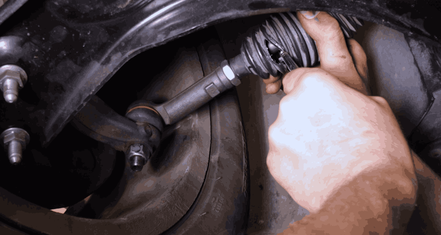 Technician inspecting a mechanical joint and rubber boot beneath a car