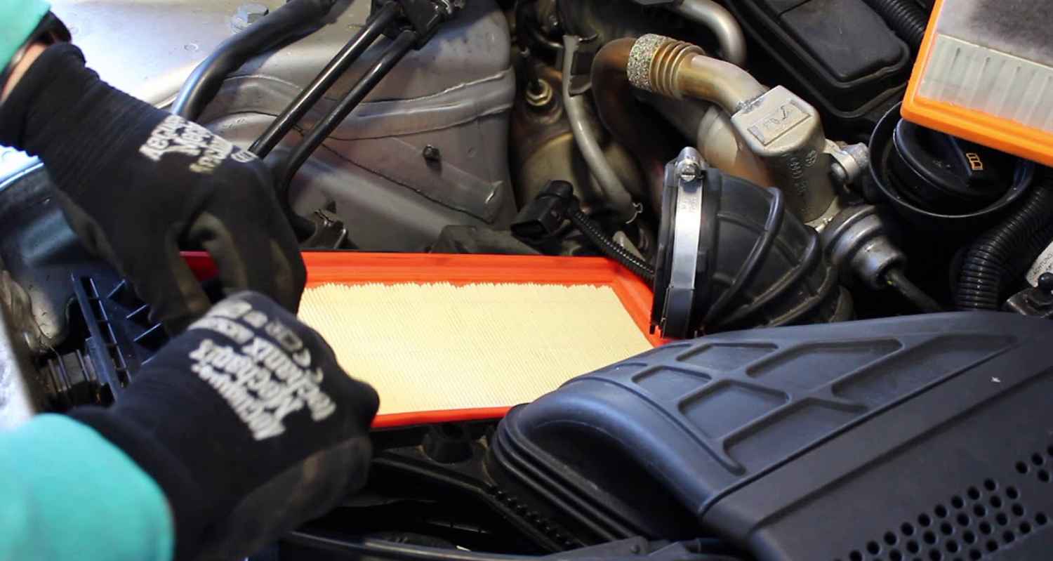 Gloved technician fitting a rectangular engine air filter in an open airbox