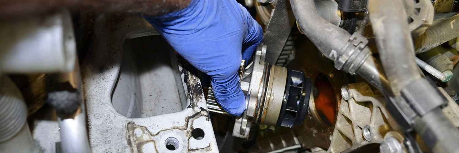 Gloved technician working around a water pump in an engine bay