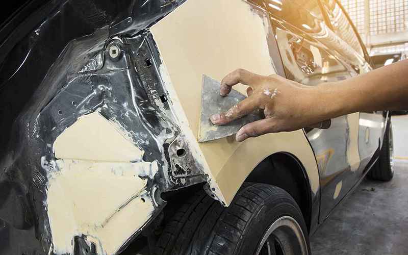 A body repair technician preparing a rear quarter panel before refinishing
