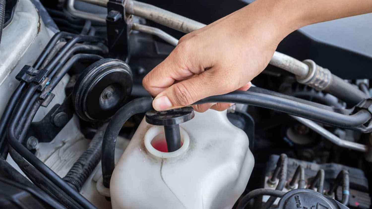 A coolant recovery bottle with a hose attached to its removable cap