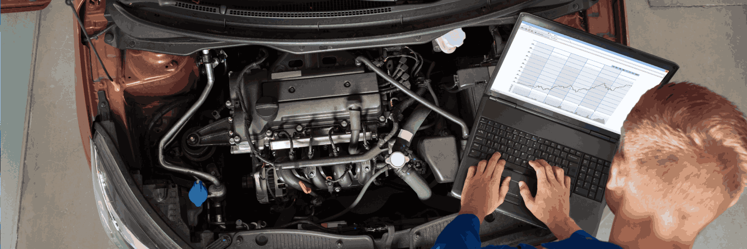 A technician viewing graphs on a laptop beside an engine