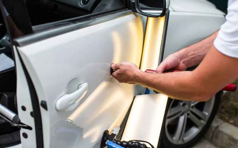 A technician using a reflection light and tools to work on a door dent