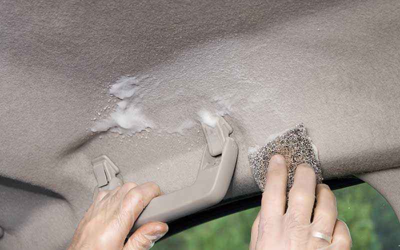 Hands working on damaged roof lining near an interior grab handle