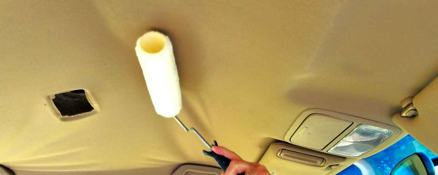 Hand holding a roller against the roof lining near the front visor