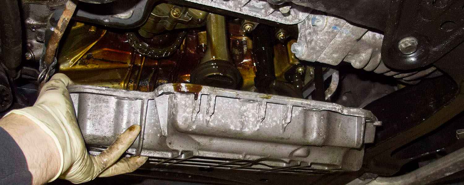 Technician supporting an oil pan beneath an engine during removal