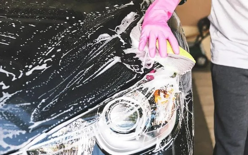 Gloved hand washing a dark car hood