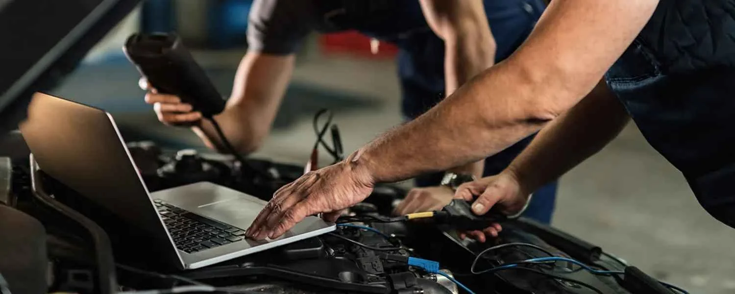 Technicians using electrical test equipment and a laptop at an open engine bay