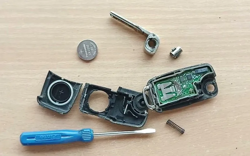 Opened car key fob with circuit board, case and battery on a workbench