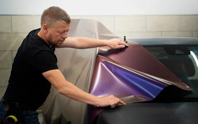 Installer positioning color-shift vinyl over a car hood