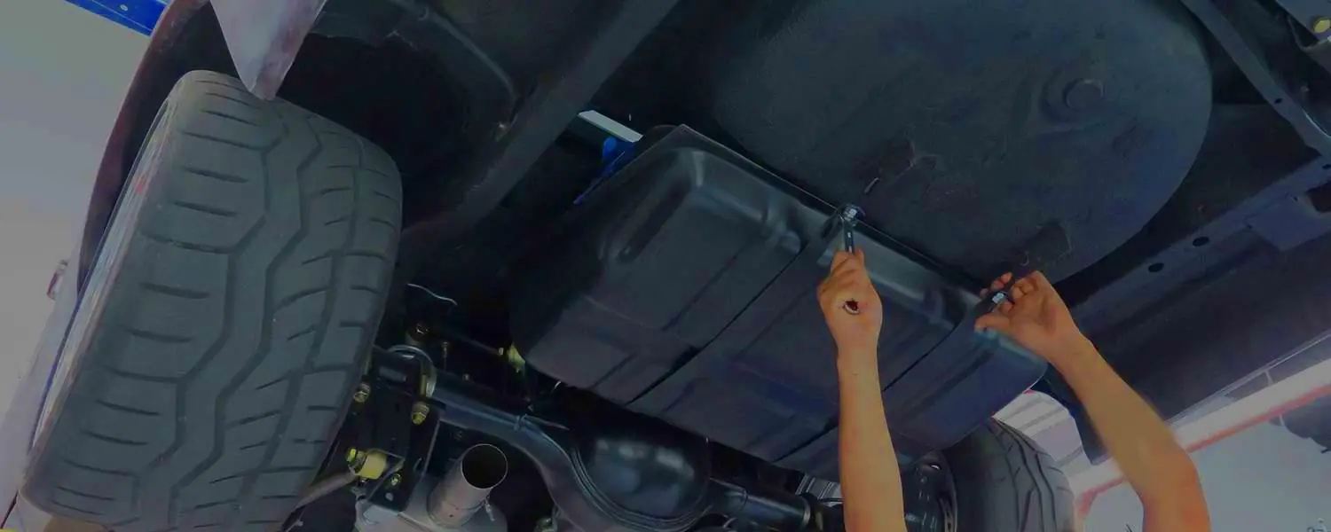 Technician accessing a fuel tank underneath a raised vehicle