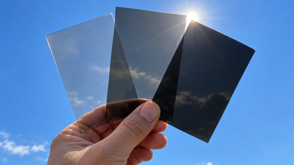 Three window tint film samples of different darkness held up against the sky